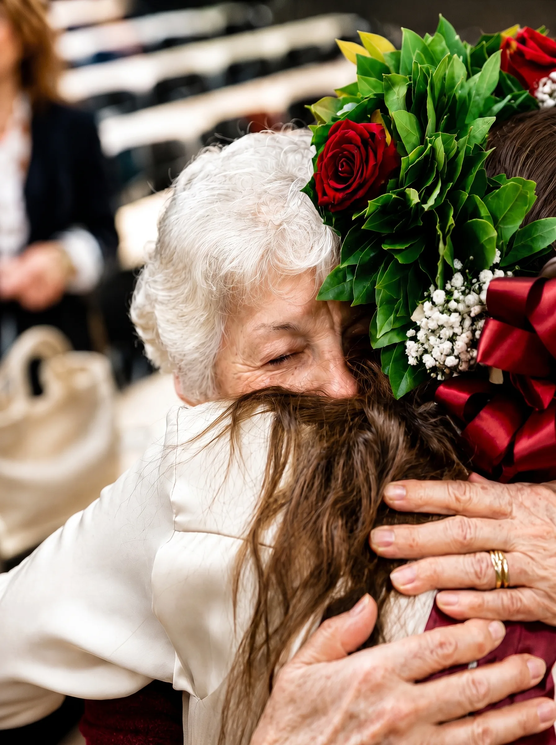 Nonna abbraccia la nipote neolaureata con la corona d'alloro e rose rosse intrecciata a mano