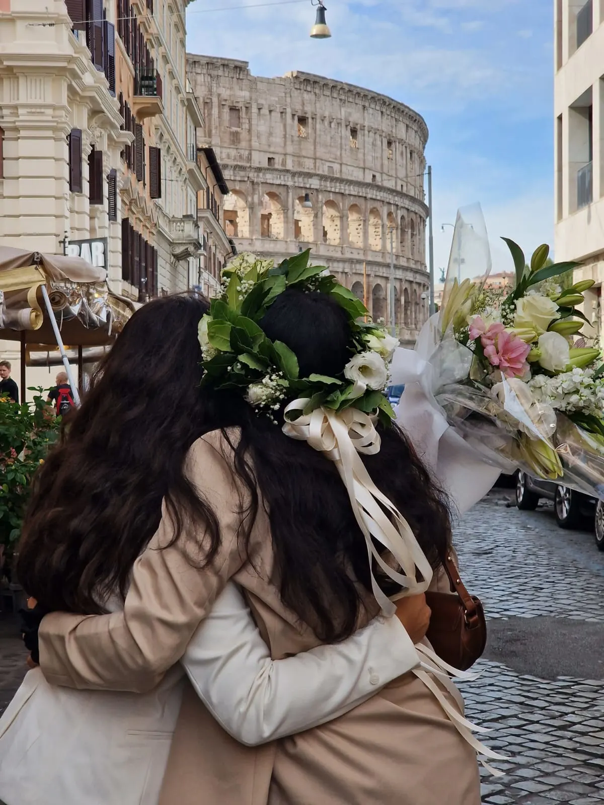 Due amiche abbracciate con coroncine di fiori e bouquet davanti al Colosseo a Roma